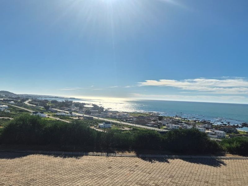 Elevated coastal view overlooking the ocean, surrounding landscape, and nearby residential development from a paved vantage point.