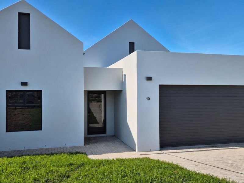 Modern contemporary house exterior featuring a clean white facade, gabled roof design, paved driveway, and an integrated double garage.
