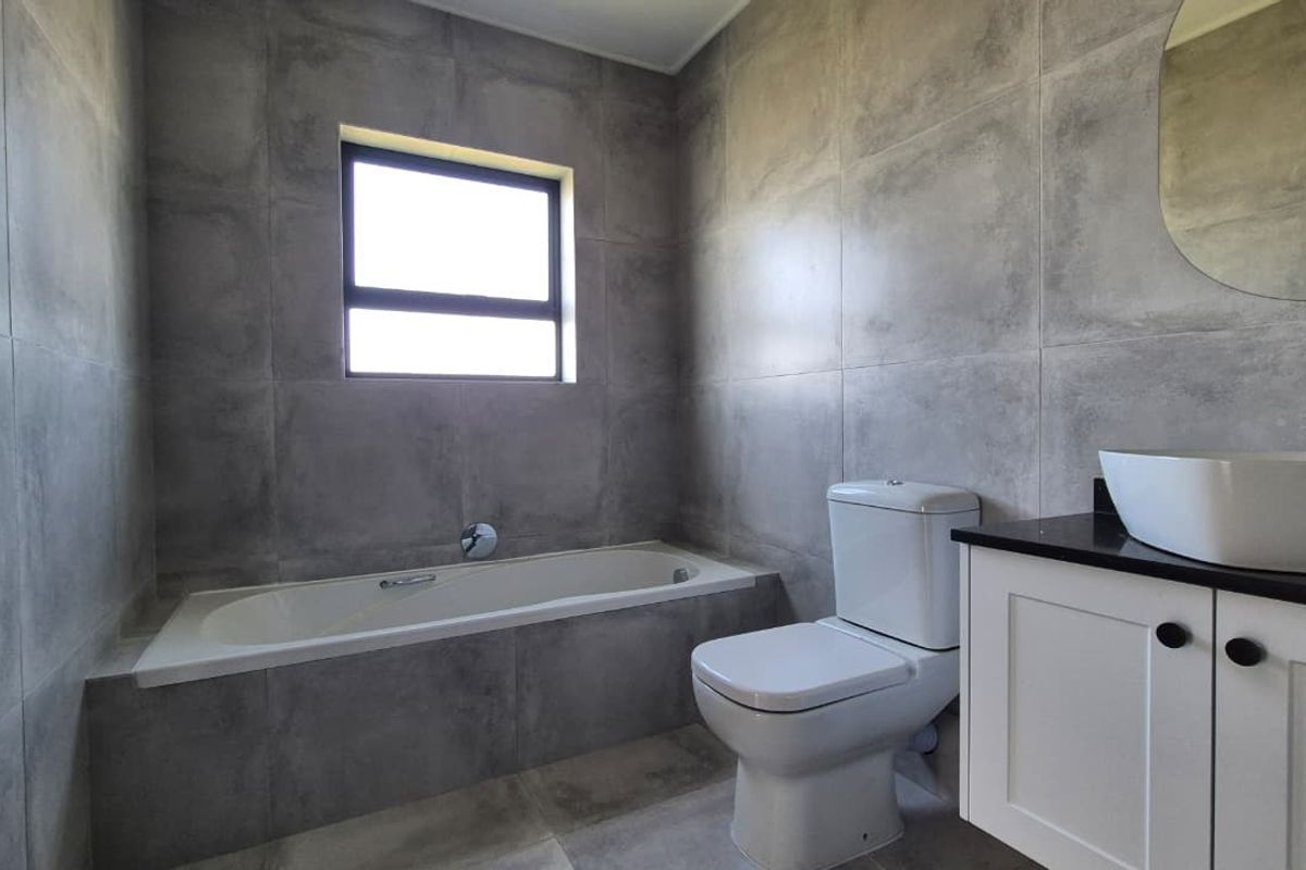 Modern bathroom featuring large-format grey wall tiles, a built-in bathtub, a white vanity with a vessel sink, and a clean, contemporary aesthetic.