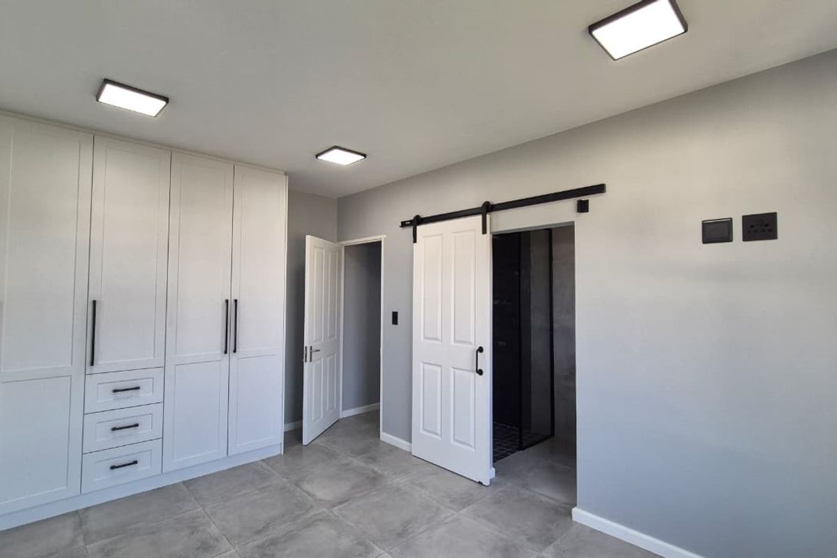 Modern bedroom featuring extensive built-in cabinetry, sleek tiled flooring, recessed lighting, and a stylish sliding barn door leading to an en-suite bathroom.