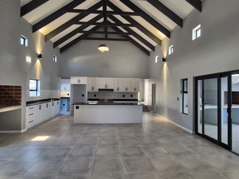 Spacious open-plan living and kitchen area featuring a high vaulted ceiling with exposed beams, modern cabinetry, a central island, and a built-in fireplace.