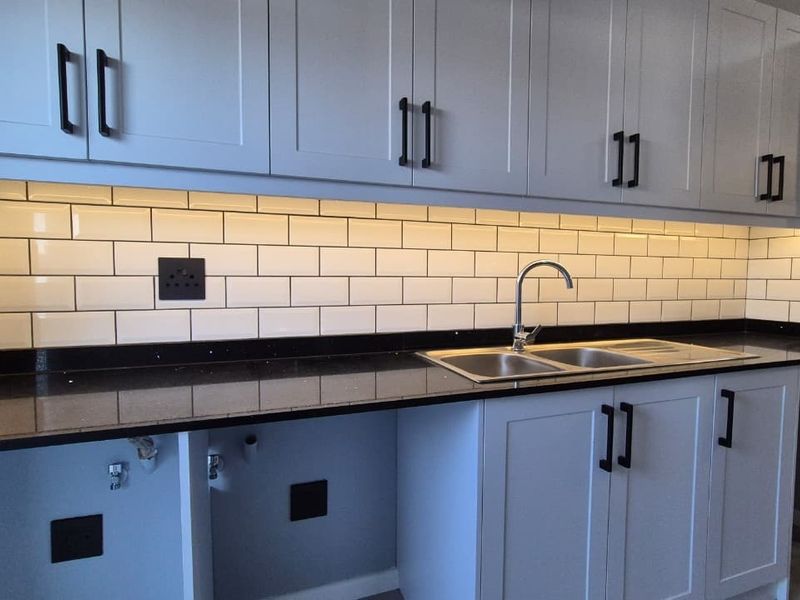 A modern, well-maintained kitchen featuring shaker-style cabinetry, a classic subway tile backsplash, black granite countertops, and a stainless steel double sink.
