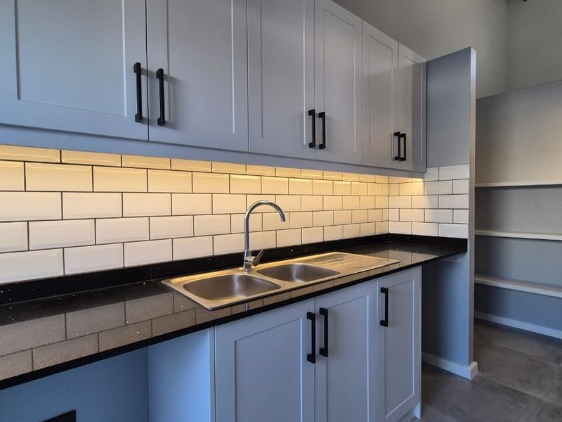 Modern kitchen featuring light grey shaker-style cabinetry, black granite countertops, a classic subway tile backsplash, and integrated under-cabinet lighting.