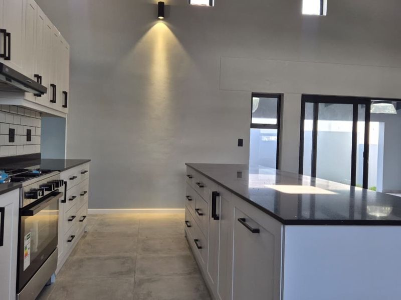 Modern kitchen featuring a large central island, stone countertops, shaker-style cabinetry, subway tile backsplash, and direct access to the outdoor area via sliding doors.