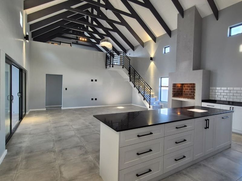 Spacious open-plan living area featuring high vaulted ceilings with exposed trusses, a modern kitchen with island, and a built-in fireplace.