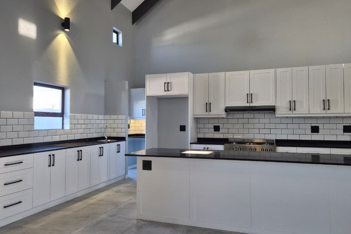 Modern kitchen featuring white cabinetry, dark stone countertops, subway tile backsplash, and a central island with a gas stove and extractor fan.