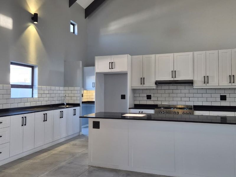 Modern kitchen featuring white cabinetry, dark stone countertops, subway tile backsplash, and a central island with a gas stove and extractor fan.