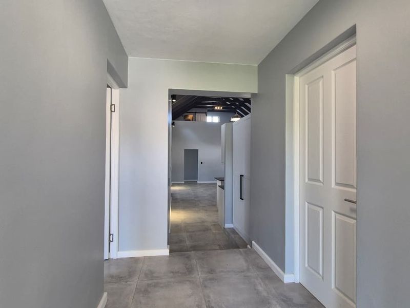 A bright, neutral-toned hallway featuring modern grey floor tiles and white panelled doors, leading into an open-plan living area.
