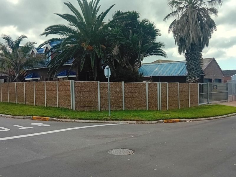 Street-level view of the property featuring a corner lot with a precast concrete boundary wall, metal gate, and established garden trees.