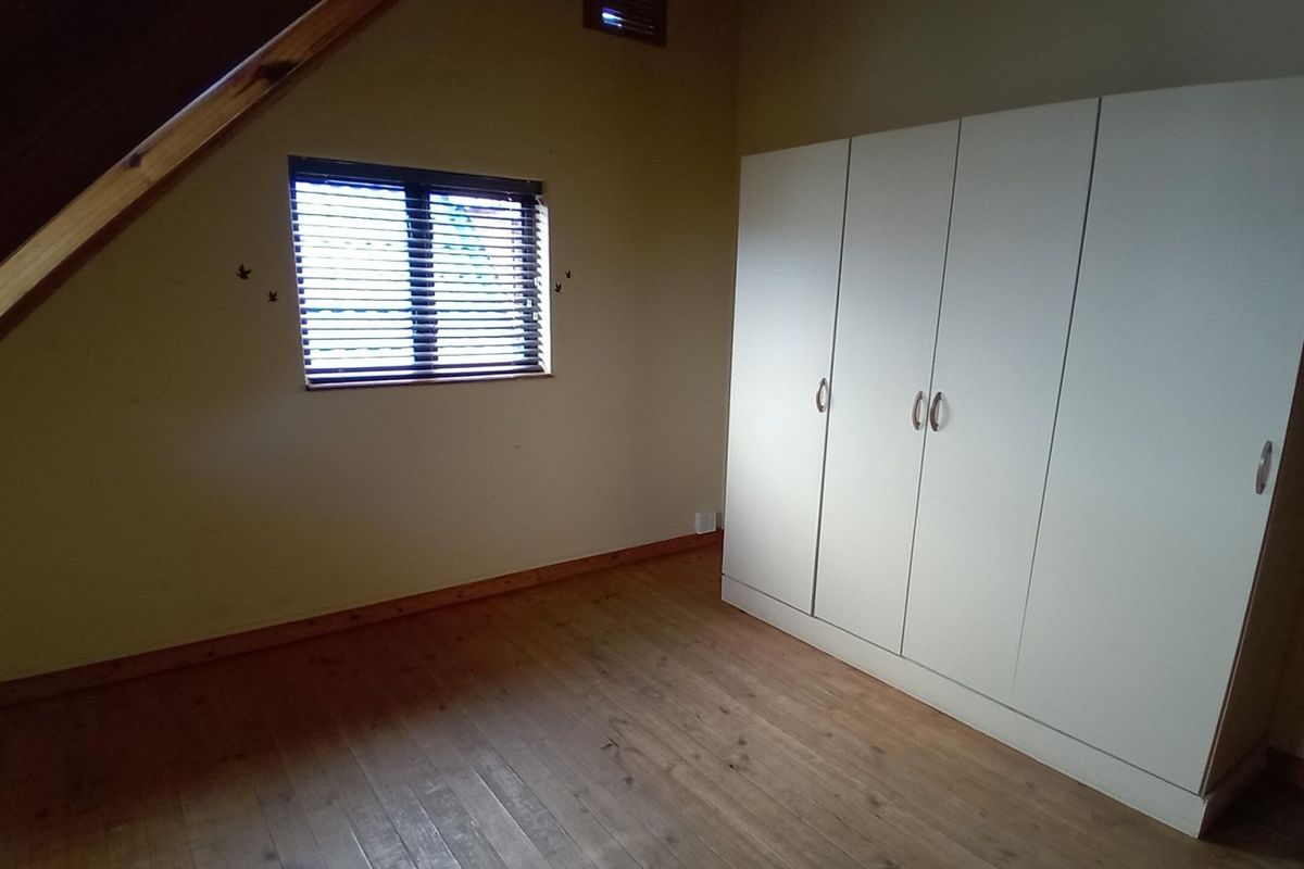 A spacious bedroom featuring timber flooring, a sloped ceiling, and a large built-in wardrobe, offering a clean and functional living space.