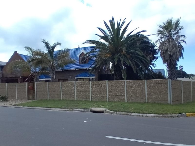 Street view of a residential property featuring a blue tiled roof, timber balcony, and a precast concrete boundary wall.