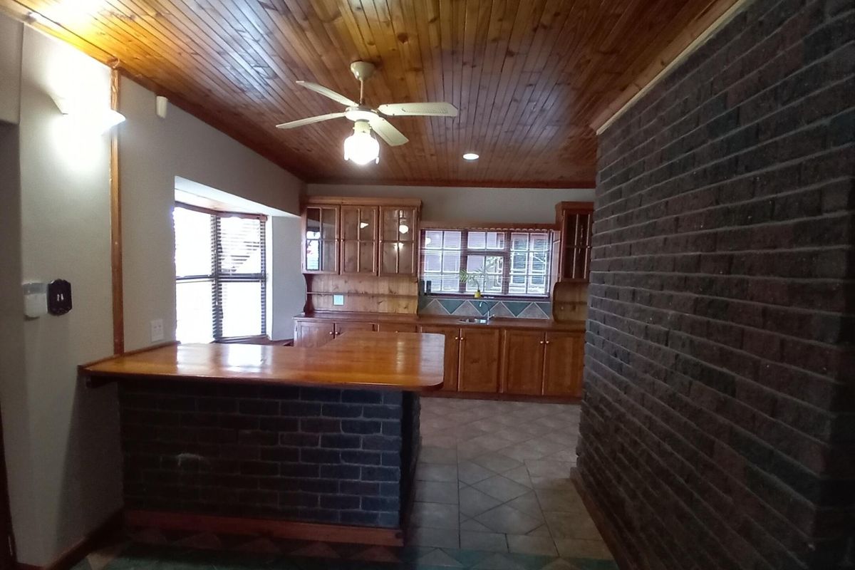 Spacious kitchen featuring wooden cabinetry, a brick breakfast bar, exposed brick feature wall, and a warm wooden tongue and groove ceiling.