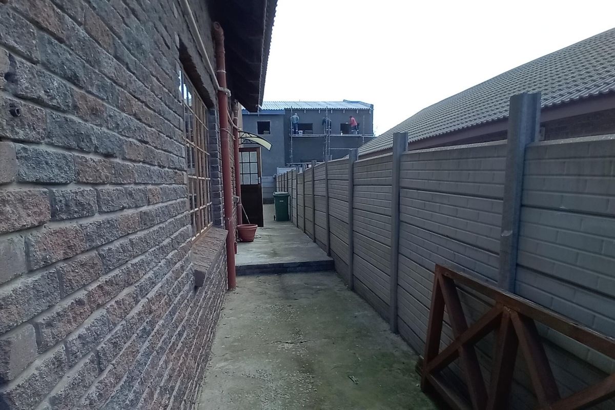 A side passage of the house featuring face brick exterior walls, a concrete walkway, and a precast concrete boundary wall.