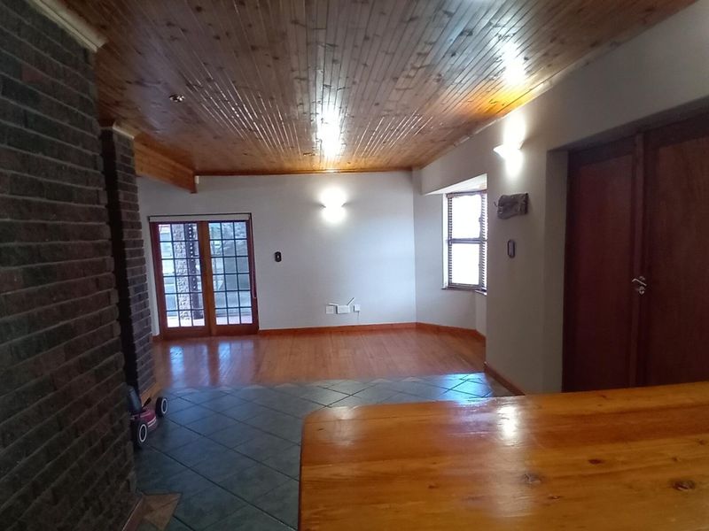 Spacious living area featuring a timber ceiling, exposed brick fireplace, and a mix of wooden and tiled flooring with access to the exterior.