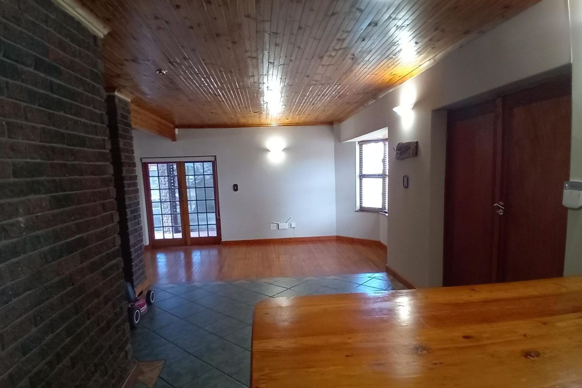 Spacious living area featuring a timber ceiling, exposed brick fireplace, and a mix of wooden and tiled flooring with access to the exterior.