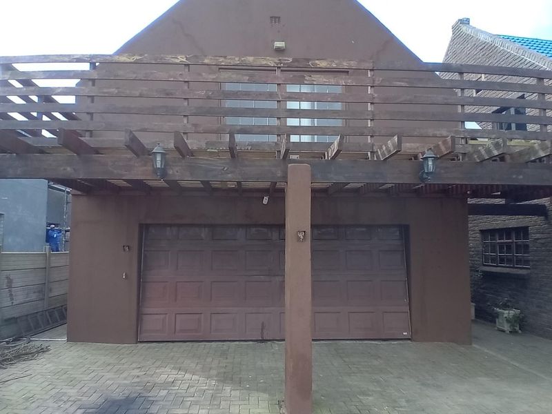 Front elevation featuring a double garage with a timber balcony and pergola structure above, set over a paved driveway area.