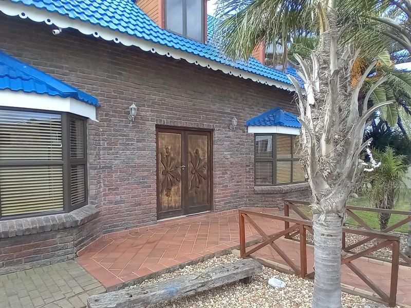 Front facade of a brick house featuring a distinctive blue tiled roof, double wooden entrance doors, and a terracotta tiled porch area.