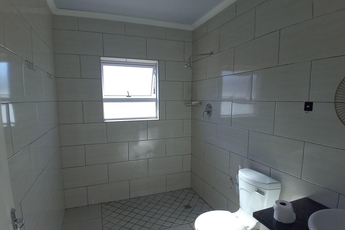A clean, modern bathroom featuring tiled walls, a walk-in shower area, a toilet, and a vanity basin.