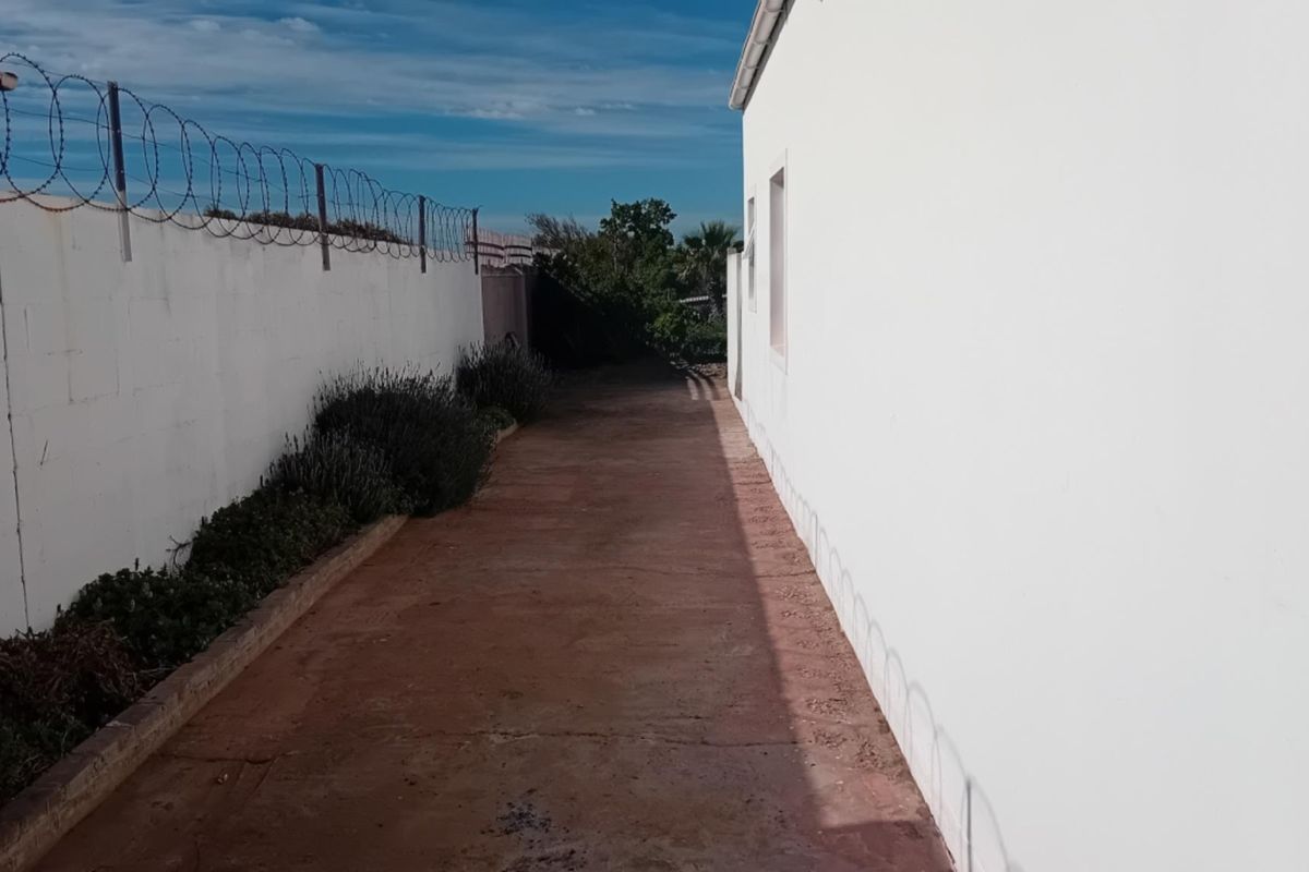 A narrow side or rear exterior pathway featuring a concrete walkway bordered by a perimeter wall with security razor wire.