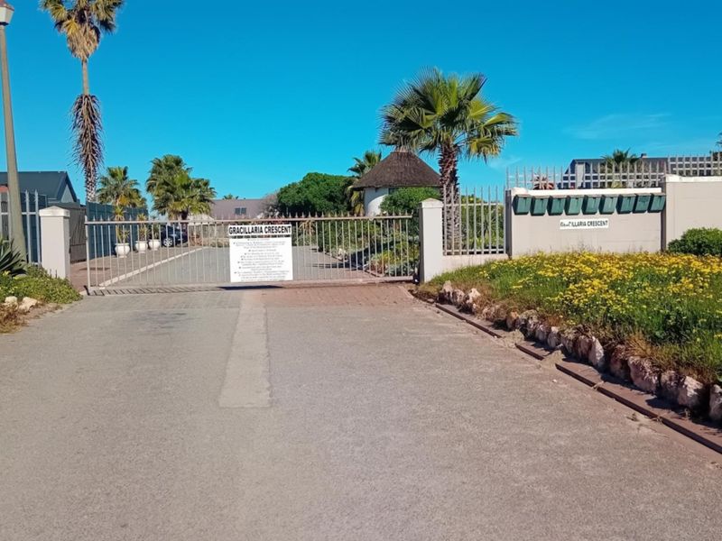 View of the secure gated entrance to the residential complex, featuring a paved driveway, perimeter wall, and communal post boxes.
