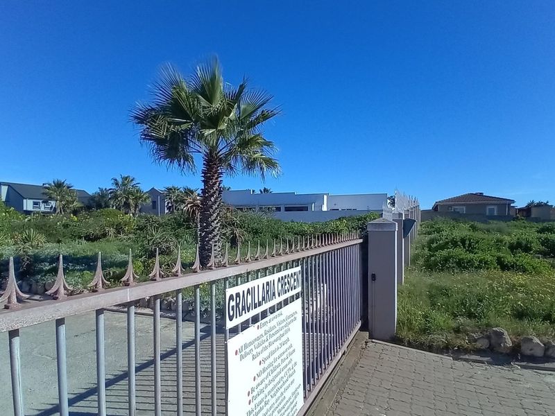 A street-level view of a residential estate entrance featuring a metal security gate and paved access road.