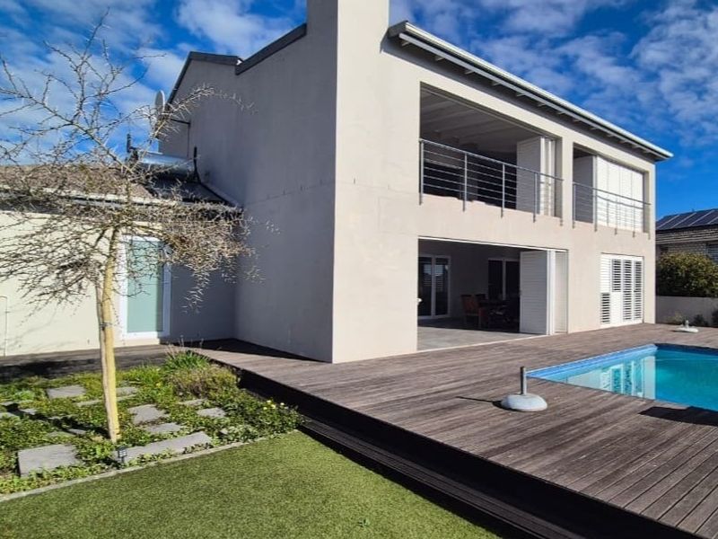 Rear view of the property featuring a swimming pool, timber decking, a covered patio, and an upper-level balcony with modern finishes.