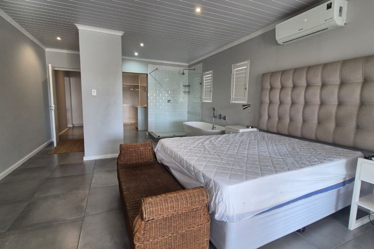 Spacious bedroom featuring an open-plan ensuite with a freestanding bathtub and glass shower, complemented by modern tiled flooring and integrated air conditioning.