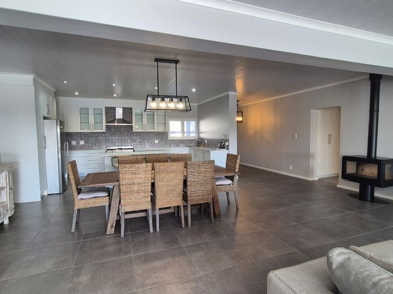 Spacious open-plan living and dining area featuring large format floor tiles, a modern freestanding fireplace, and a well-appointed kitchen with contemporary cabinetry.