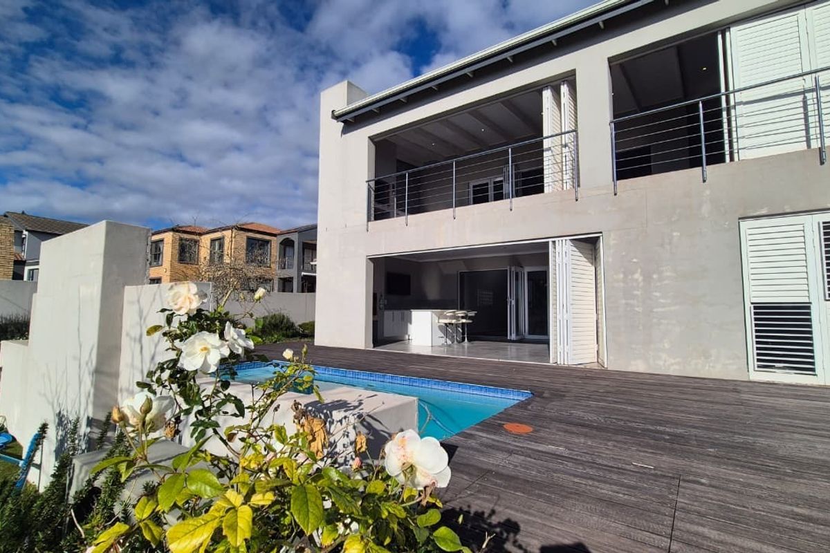 Rear exterior view featuring a swimming pool, timber decking, and a covered patio with folding doors leading to an upper-level balcony.