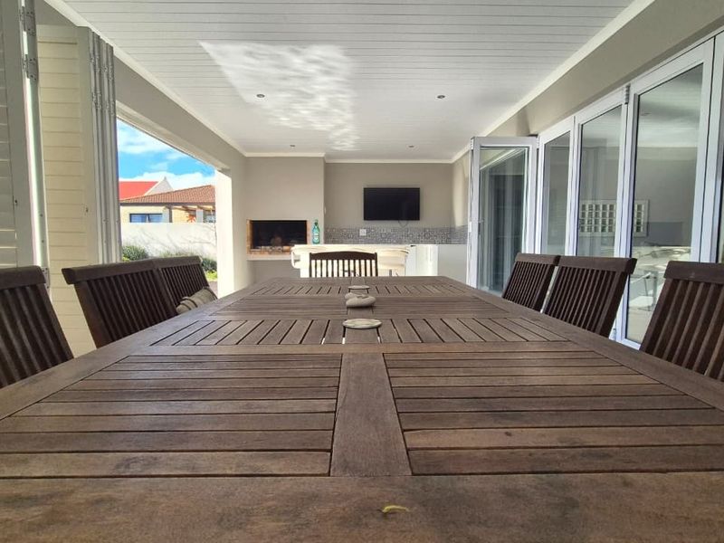 Spacious covered patio featuring a built-in braai, recessed lighting, and large bi-fold doors that seamlessly connect the indoor and outdoor living areas.