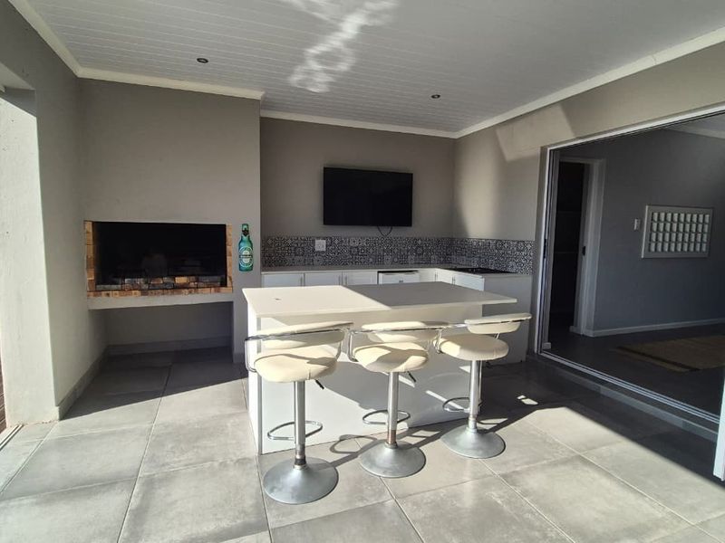 Covered outdoor patio featuring a built-in braai, kitchen island with seating, and bi-fold doors connecting to the interior living space.