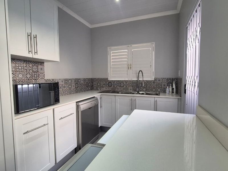 A clean, modern kitchen featuring white cabinetry, patterned tile backsplash, stone-look countertops, and a stainless steel sink with a security gate at the entrance.