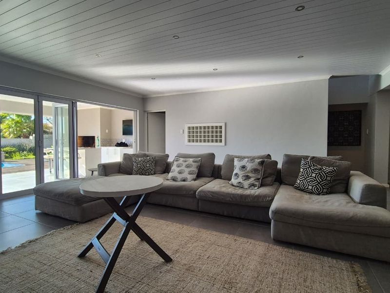 Spacious living room featuring a timber panelled ceiling, recessed lighting, and large bi-fold doors opening to an outdoor pool area.