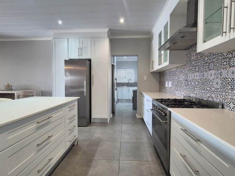 Modern kitchen featuring a central island, gas cooktop with extractor, quartz countertops, and stylish patterned tile backsplash with ample shaker-style cabinetry.