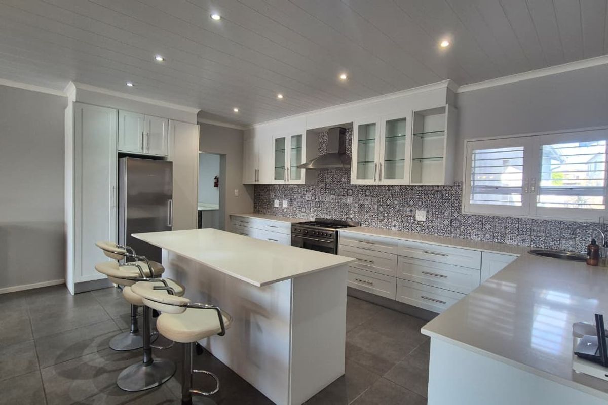 Modern kitchen featuring white cabinetry, quartz countertops, a central island, gas stove, and decorative tiled backsplash with recessed lighting.