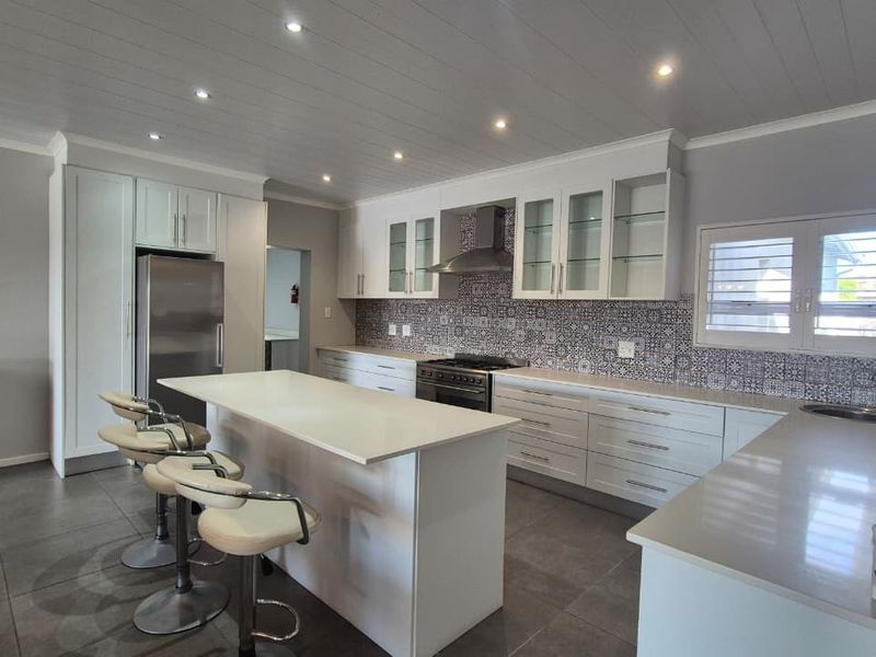 Modern kitchen featuring white cabinetry, quartz countertops, a central island, gas stove, and decorative tiled backsplash with recessed lighting.