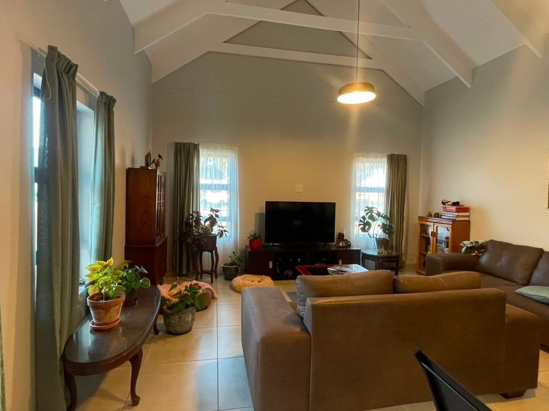 Spacious living room featuring a high vaulted ceiling with exposed rafters, tiled flooring, and ample natural light from multiple windows.