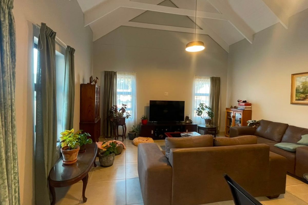 Spacious living room featuring a high vaulted ceiling with exposed rafters, tiled flooring, and ample natural light from multiple windows.