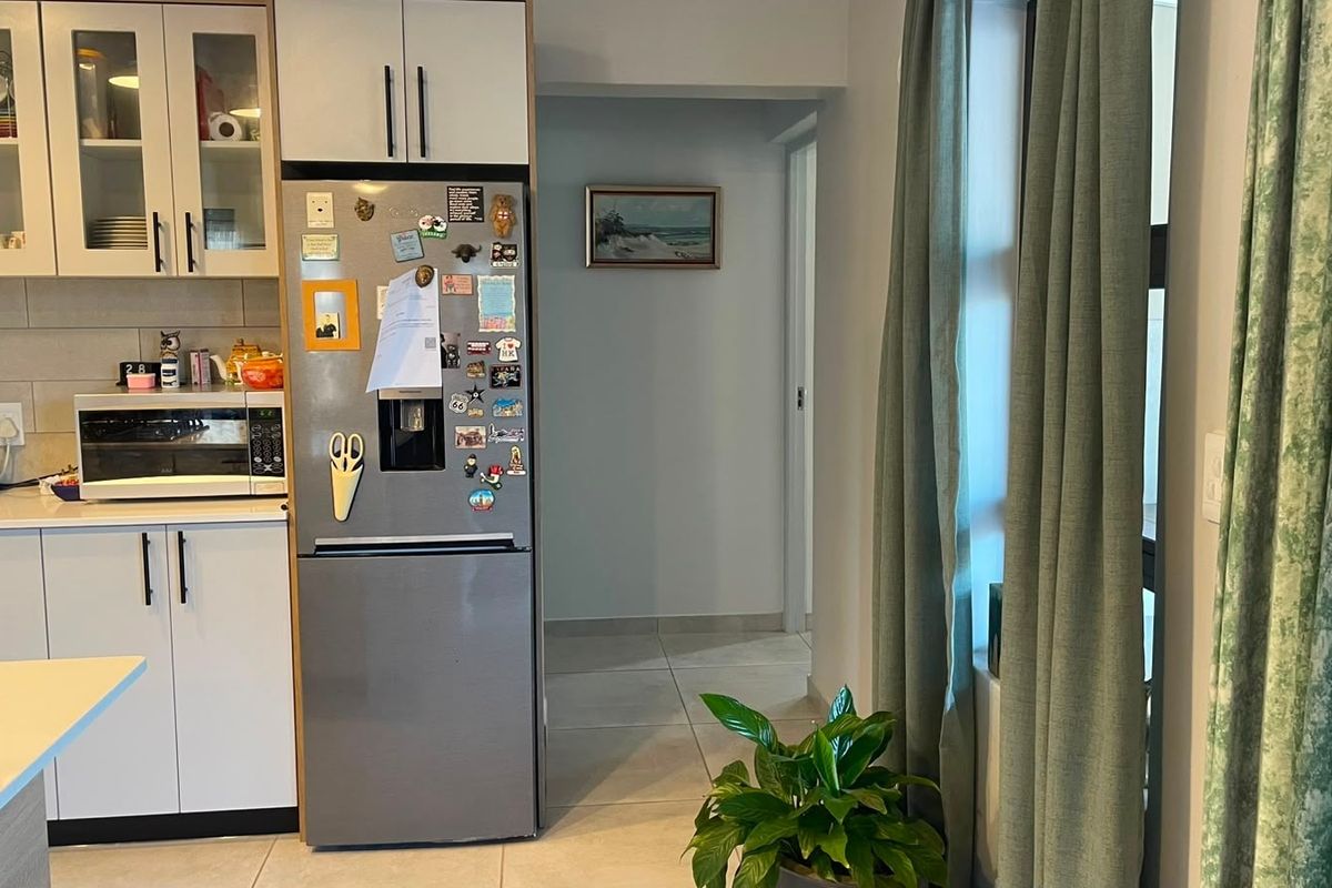 A functional kitchen area featuring white built-in cabinetry, a tiled backsplash, and neutral floor tiles, leading into a hallway.