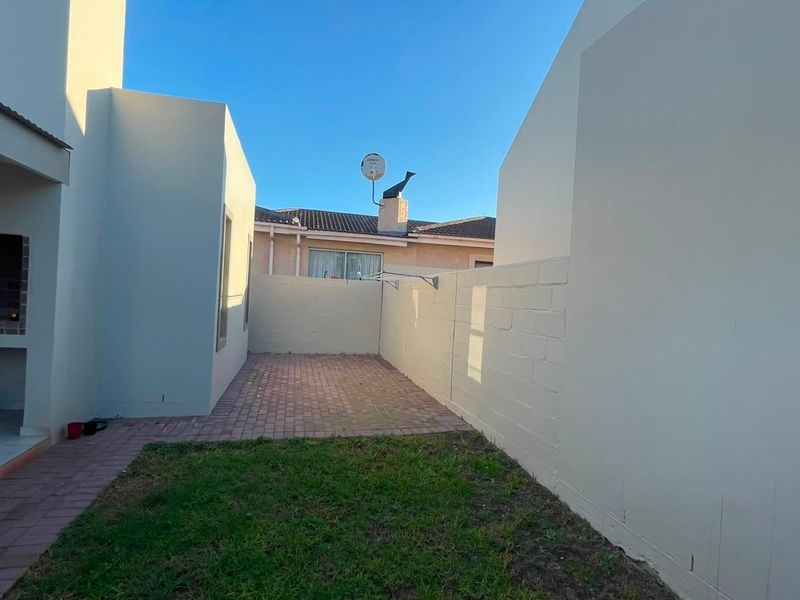 A private rear courtyard featuring a paved patio area, a built-in braai, and a small lawn, enclosed by high boundary walls.