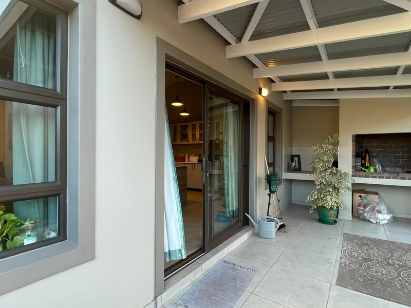Covered patio area featuring tiled flooring, exposed beam ceiling, and a built-in brick braai, providing a functional outdoor entertainment space.
