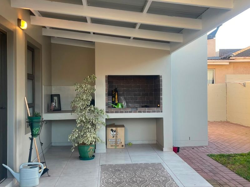 Covered patio area featuring a built-in brick braai, tiled flooring, and direct access to the rear garden and paved outdoor space.