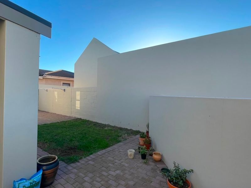 A private rear courtyard featuring brick paving, a small lawn area, and a built-in braai structure.