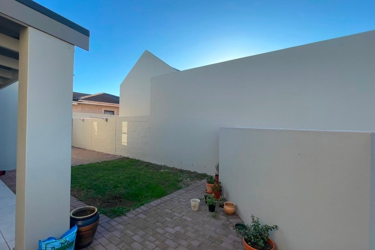 A private rear courtyard featuring brick paving, a small lawn area, and a built-in braai structure.