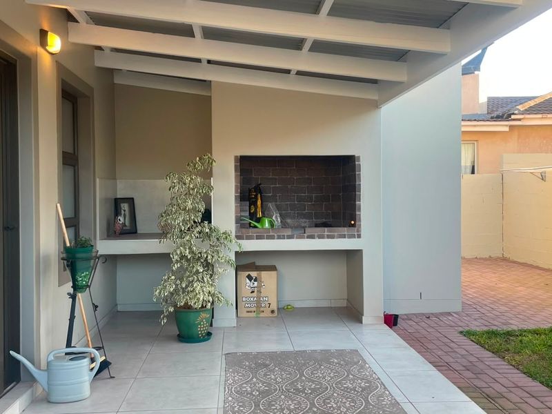 Covered patio area featuring a built-in brick braai and tiled flooring, providing a functional outdoor entertainment space.