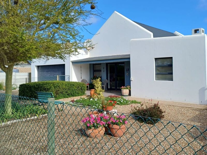 A well-maintained single-story house featuring a clean white facade, gabled roof, integrated garage, and a neat front garden with a paved entrance area.