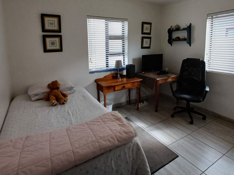 A functional bedroom featuring tiled flooring and dual windows with venetian blinds, offering a neutral space ready for personalization.