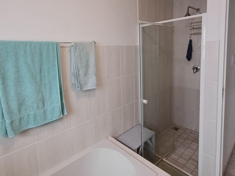 A functional bathroom featuring a bathtub, a separate shower enclosure with glass door, and neutral wall tiling.