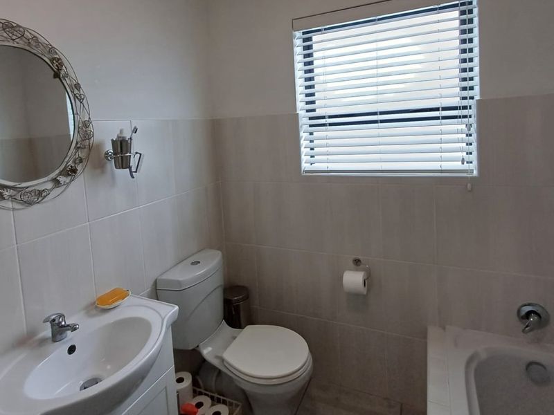 A functional bathroom featuring a vanity basin, toilet, and bathtub with neutral wall tiling and venetian blinds.
