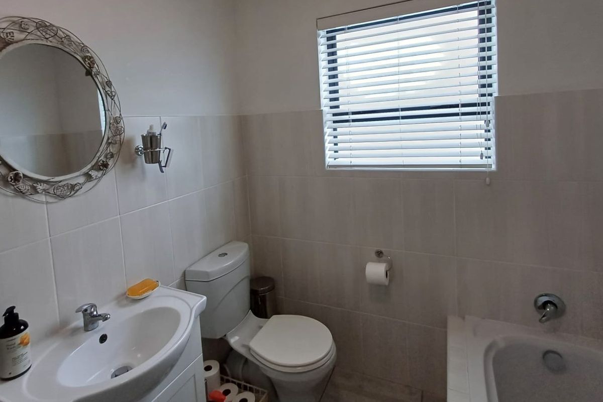 A functional bathroom featuring a vanity basin, toilet, and bathtub with neutral wall tiling and venetian blinds.